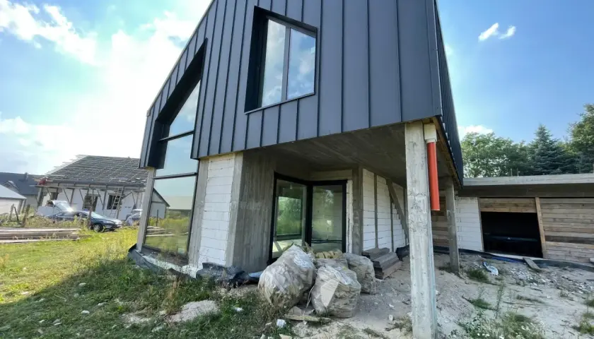 Nowoczesny dom w budowie z szarym dachem i dużymi oknami.