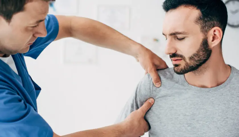 Fizjoterapeuta bada bark pacjenta, który odczuwa ból. Objawy uszkodzenia barku mogą być różne.