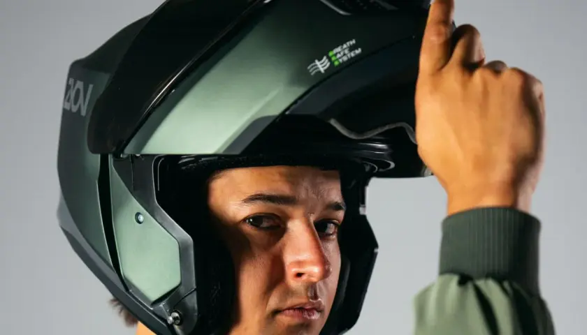Un hombre se ajusta un casco de moto verde oscuro, similar a un casco guardia civil, con el sistema "Breath Safe" visible.