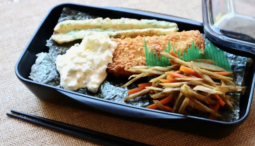 A delicious nori bento box with fried fish, creamy potato salad, and stir-fried vegetables.