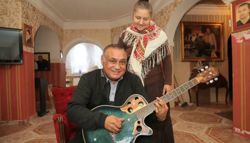 Don Vasyl siedzi z gitarą, obok niego stoi kobieta w chustce.