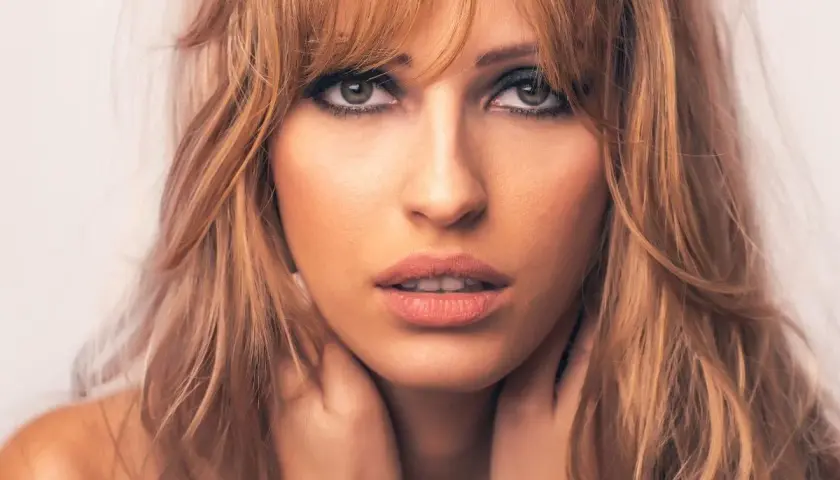 Kobieta z blond włosami i cieniowaniem grzywki, z dłońmi na szyi.