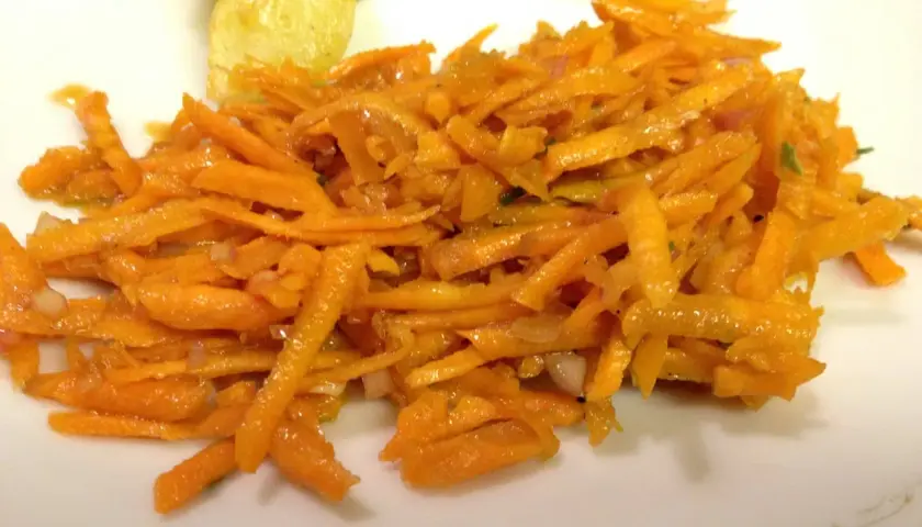 En fransk morotssallad med finstrimlad morot, lök och en lätt dressing. Serveras på en vit tallrik.