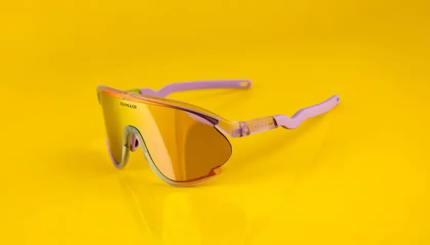 Oto odpowiedź na pytanie: jakie okulary na rower? Stylowe, pomarańczowe okulary sportowe z fioletowymi zausznikami, idealne na rowerową przejażdżkę.