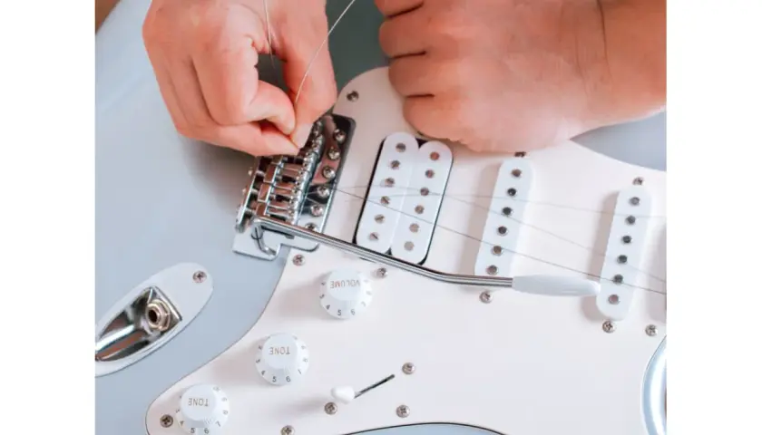 Ręce montują nową strunę w gitarze elektrycznej. Dowiedz się, co ile wymieniać struny w gitarze elektrycznej, by cieszyć się czystym brzmieniem.