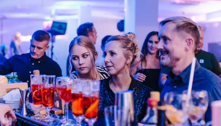 Ludzie przy barze, na pierwszym planie drinki, w tle niebieskie światła.