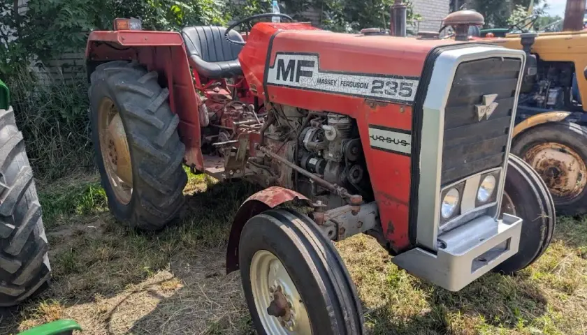 Czerwony Massey Ferguson 235 z napisem "Ursus" na masce, gotowy do pracy na polu.