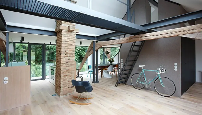 Moderner offener Dachstuhl mit sichtbaren Stahlträgern, Ziegelpfeiler, Holz und einer Leiter. Ein Fahrrad steht bereit.