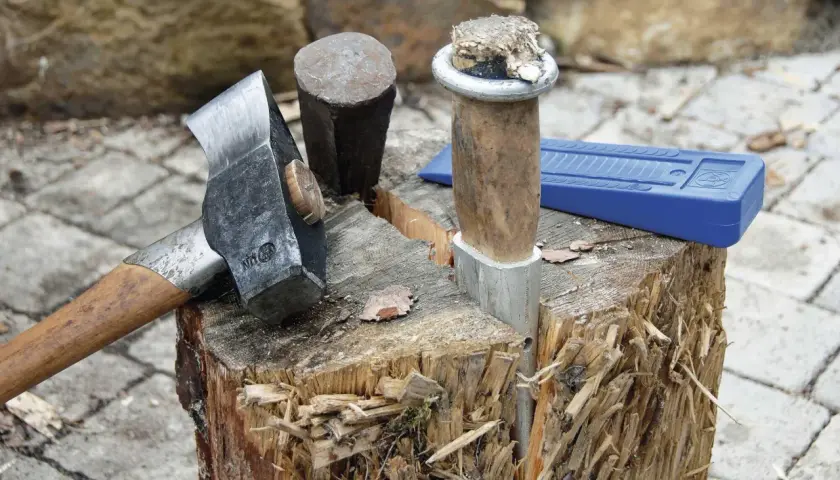 Werkzeuge zum Birken spalten: Beil, Spalthammer und Keil liegen bereit. Ein Holzstamm ist bereits angespalten.