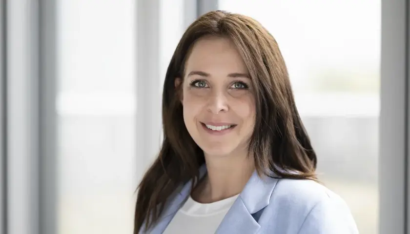 Porträt einer lächelnden Frau mit braunen Haaren und einem hellblauen Blazer. Dies ist eine klare Definition eines Porträts.