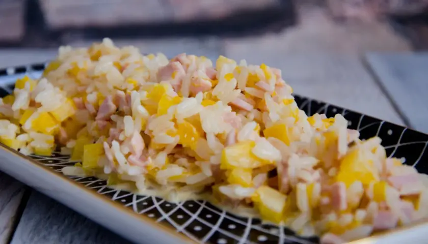 Reissalat mit Mandarinen und Schinken, cremig und fruchtig, auf einem dekorativen Teller serviert.