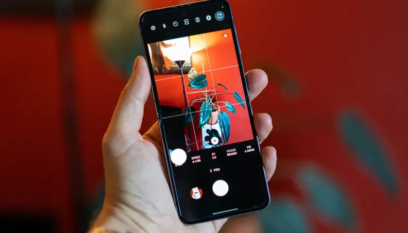 Dłoń trzyma smartfon z włączonym trybem Pro, ukazującym roślinę w doniczce. To jak przenośny Lightroom na telefon, gotowy do edycji.