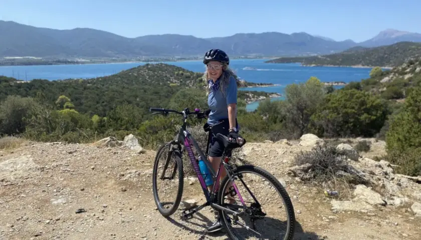 Woman on a bicycle enjoying scenic bicycle tours over 50, with a beautiful blue bay and mountains in the background.