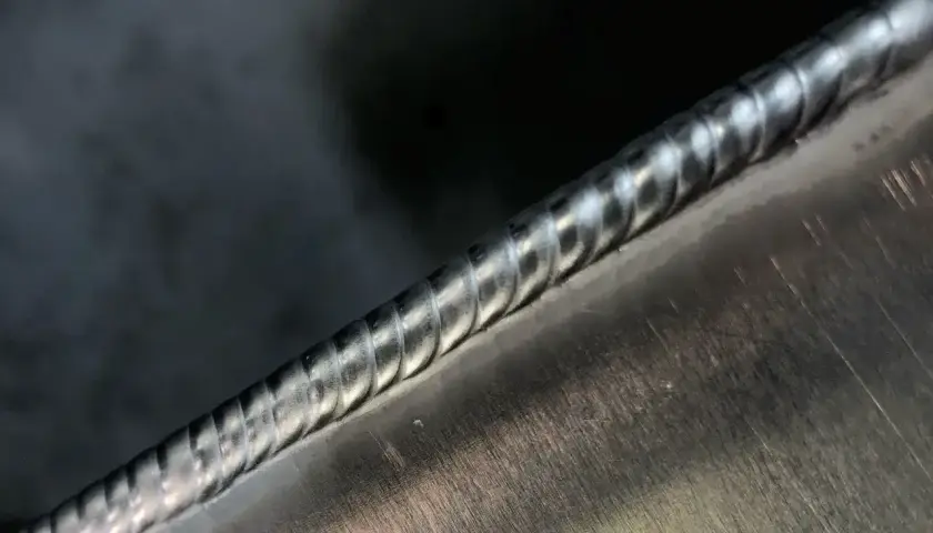 Zbliżenie na idealnie wykonaną spoinę spawalniczą na metalowej powierzchni.