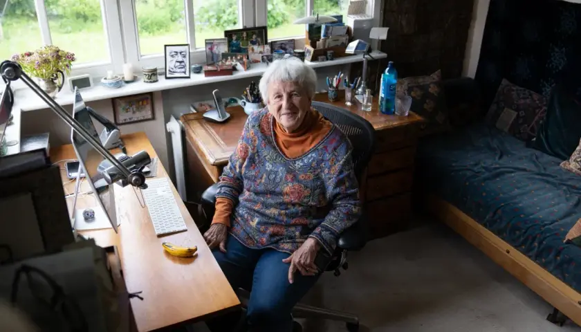 Ingrid Noll sitzt an ihrem Schreibtisch, umgeben von Erinnerungen und Inspirationen für ihre Geschichten über Kinder.