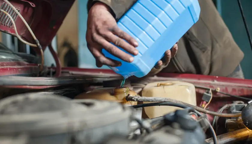 Mecánico vierte líquido refrigerante azul para limpiar radiador coche.