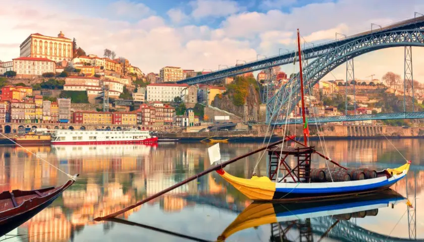Barcos tradicionales navegan por el río Duero, con la colorida Ribeira y el puente Dom Luís I al fondo. Perfectas rutas cerca de Oporto para explorar.