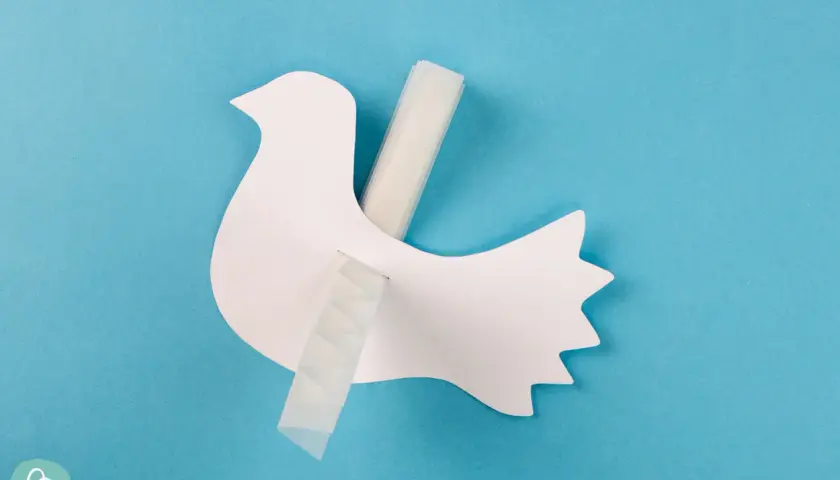 Eine weiße Papier-Friedenstaube wird mit Klebeband befestigt. Bastelanleitung für eine Friedenstaube.