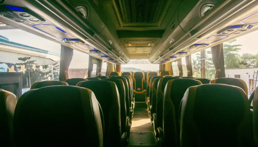 Wnętrze autobusu z rzędami ciemnych siedzeń i niebieskim oświetleniem podsufitowym.