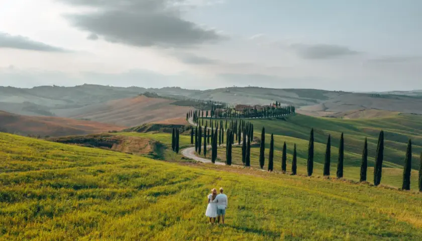 A couple enjoys the view of rolling hills and a cypress-lined road, perfect for renting a car in Tuscany.