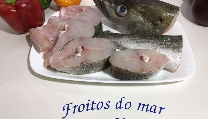 Rodajas de abadejo pescado fresco en plato blanco, junto a pimientos y el texto "Froitios do mar San Simón".