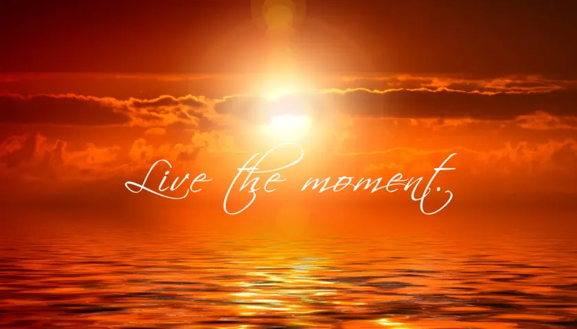 Tramonto infuocato sull'oceano, con la scritta "Live the moment" che invita a vivere il presente.