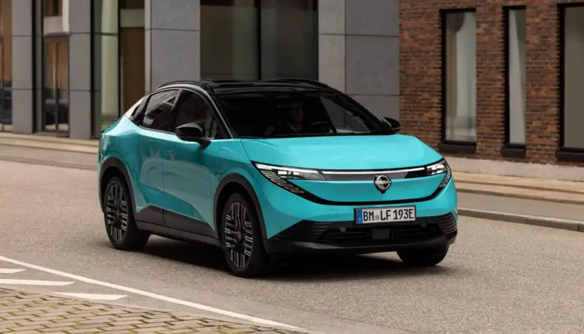 La Nissan Leaf 2026, in un vivace color acquamarina, sfreccia su una strada urbana, con un design futuristico che cattura l'attenzione.