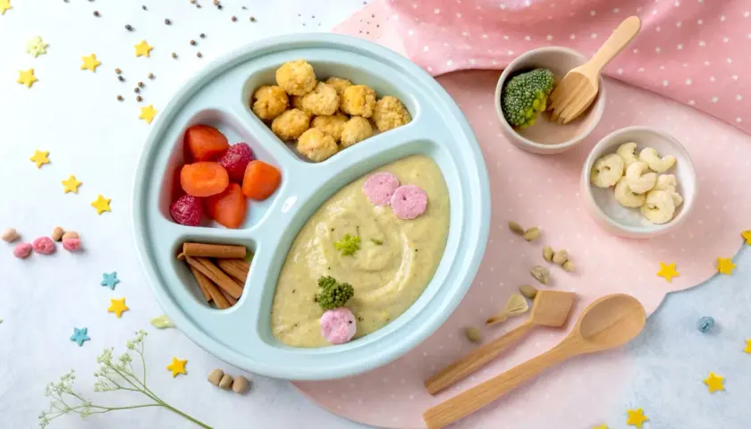 Kolorowy talerzyk z jedzeniem dla malucha: puree z warzyw, marchewka, maliny, chrupki i brokuł. Idealny na blw pierwszy posiłek.