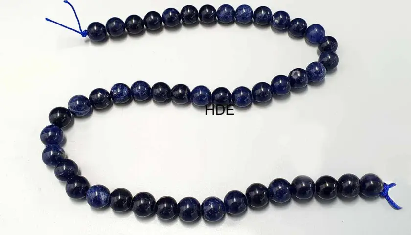 Eine Kette aus tiefblauen Sodalith-Perlen, die auf einem weißen Hintergrund liegen.