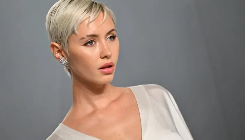Krótkie, blond włosy i wyraziste rysy twarzy. Stylizacja z błyszczącą biżuterią, idealna jako inspiracja fryzury dla grubych twarzy.