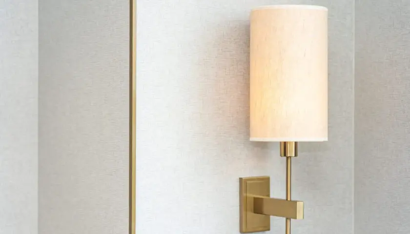 Aplique de pared moderno con pantalla de tela beige, montado en una pared con textura gris.
