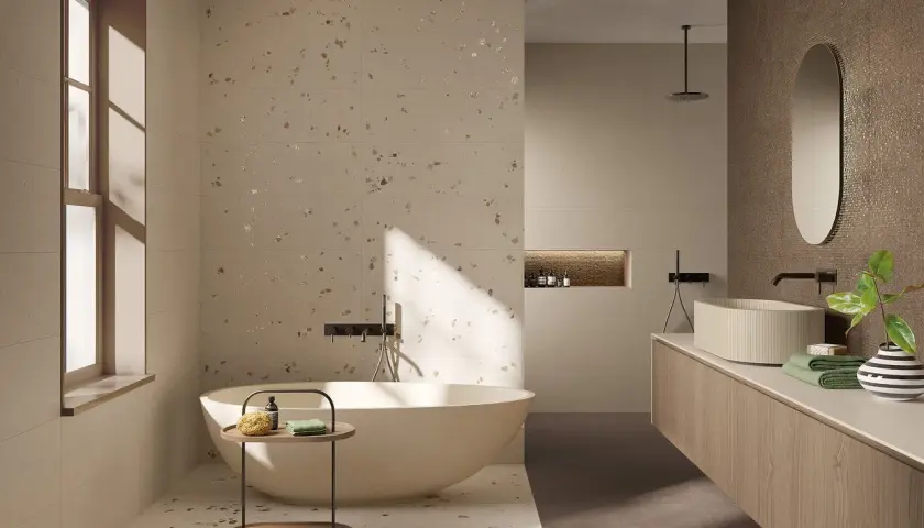 Bagno moderno con vasca freestanding e lavabo su mobile sospeso. Pareti e pavimento in fap gres porcellanato effetto terrazzo con inserti metallici.