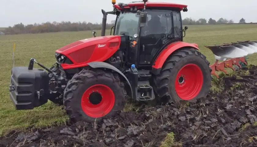 Czerwony ciągnik Zetor 6245 z pługiem orze pole w pochmurny dzień.