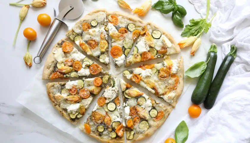 Gesunder pizzateig mit Zucchini, Kirschtomaten und Mozzarella, garniert mit Basilikum und Zucchiniblüten.