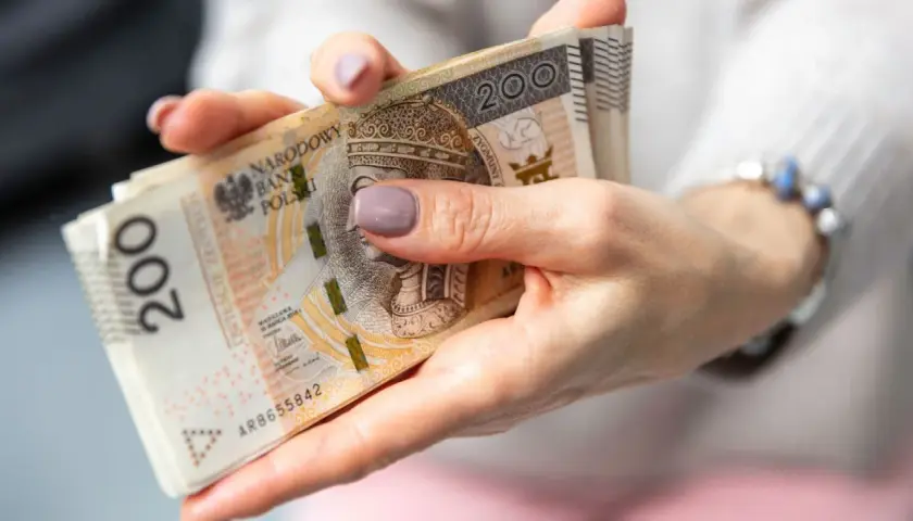 Dłonie trzymające stos banknotów 200 zł. Czas oczekiwania na wypłatę emerytury po złożeniu wniosku.