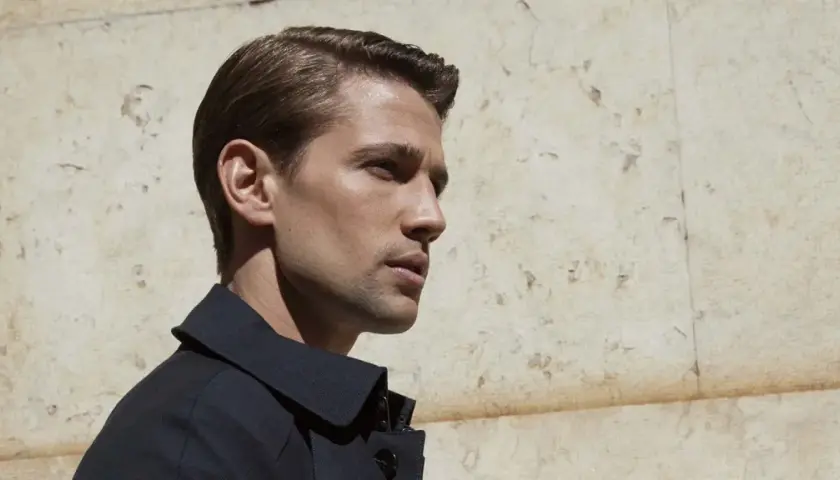 Hombre con corte de pelo con raya, peinado hacia atrás con gel, luciendo elegante y moderno.