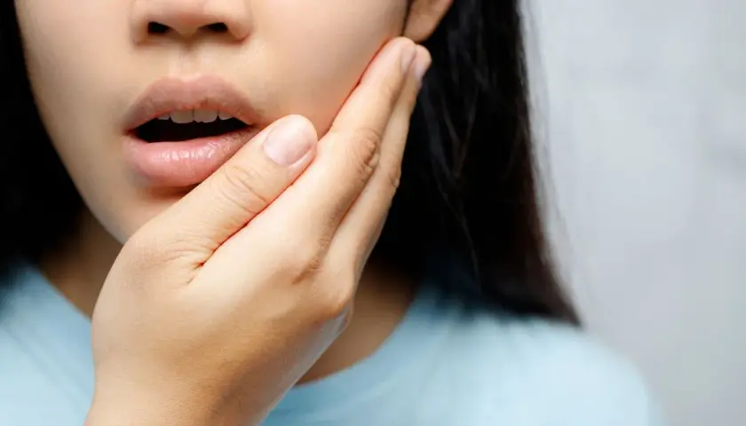 Mujer con mano en la mejilla, experimentando dolor de dientes al quitar Invisalign.