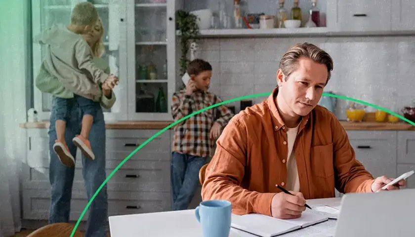 Mężczyzna w pomarańczowej koszuli pracuje przy laptopie, podczas gdy rodzina jest w tle.