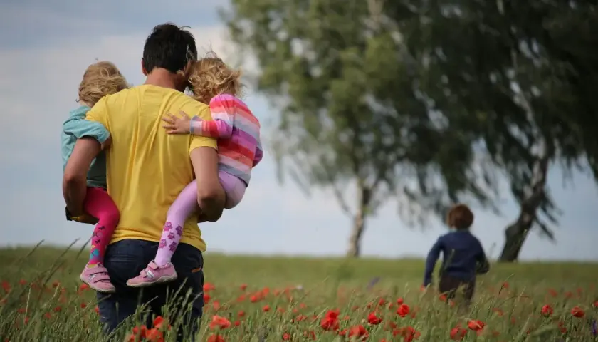 Un padre porta in braccio le sue due figlie in un campo di papaveri, un'immagine che cattura la psicologia del rapporto padre e figlia.