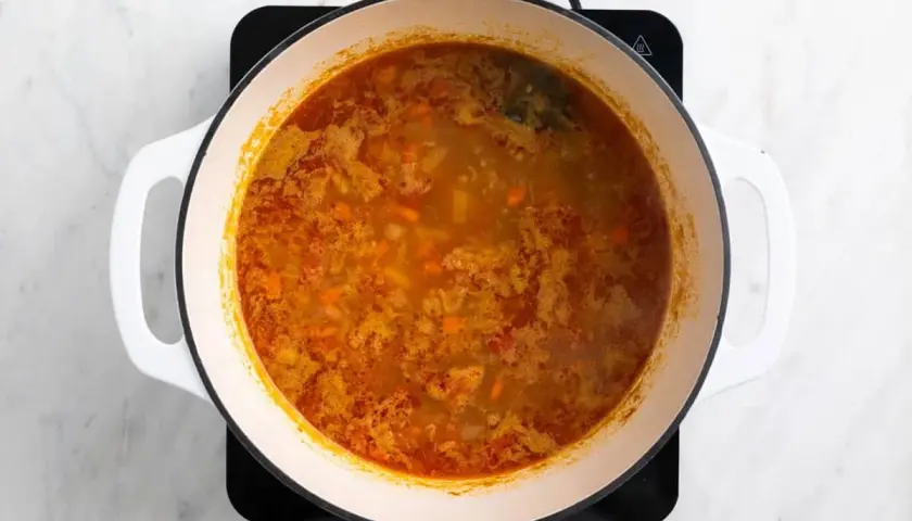 Olla con garbanzos y acelgas hirviendo, con trozos de zanahoria y especias.