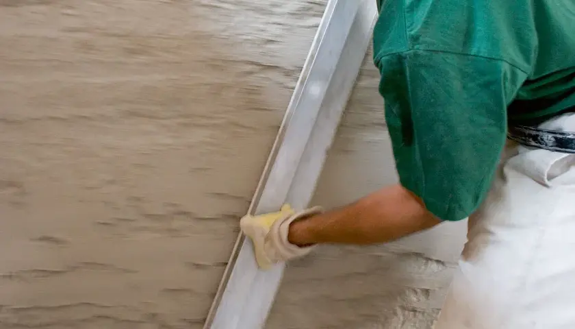 Hand mit Handschuh glättet feuchten Putz. Spezialputz gegen Feuchtigkeit schützt die Wand.