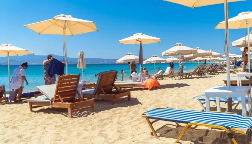 Słoneczny dzień na plaży Naxos. Leżaki pod parasolami, turkusowa woda i góry w tle.