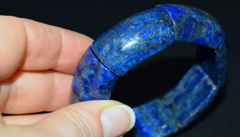 Dłoń trzyma bransoletkę z lapis lazuli, kamienia o intensywnym niebieskim kolorze i złotych inkluzjach.