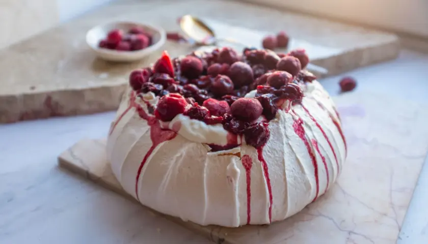 Pyszny tort pavlova z bitą śmietaną i wiśniami, ozdobiony krwistoczerwonym sosem.