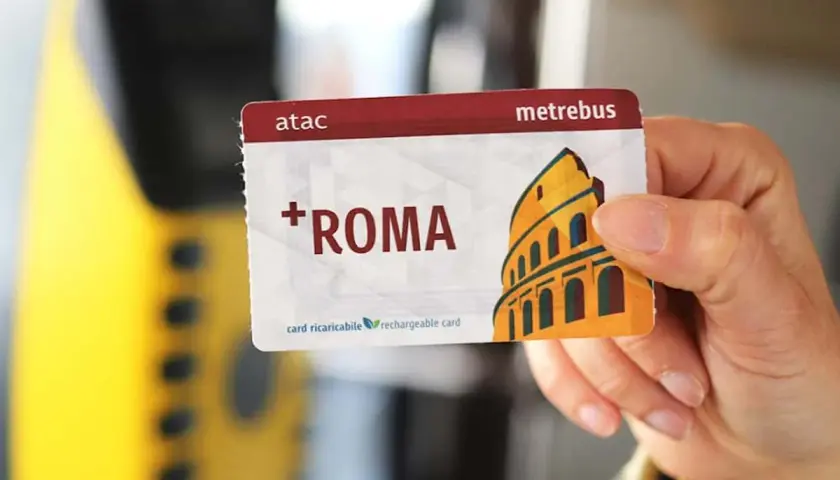 Una mano tiene una tessera metropolitana Roma con il Colosseo stilizzato. La carta è ricaricabile e riporta il logo ATAC.