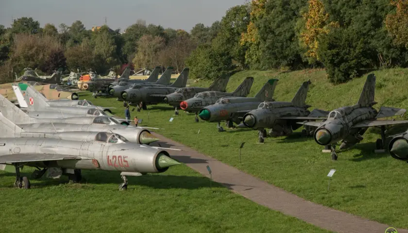 Samoloty wojskowe na trawie w Muzeum Lotnictwa w Krakowie. Widać myśliwce MiG-21 i inne maszyny.