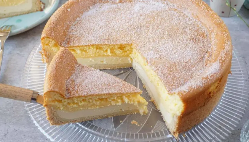 Saftige eierschecke ohne boden, mit Puderzucker bestäubt, auf einem Tortenteller. Ein Stück wurde bereits herausgeschnitten.