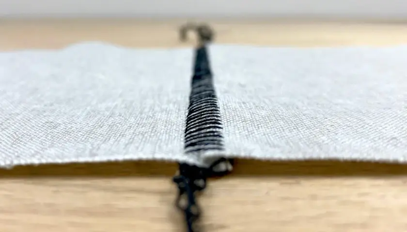 Close-up of a black stitch on white fabric, showing the difference between flatlock and coverstitch techniques.