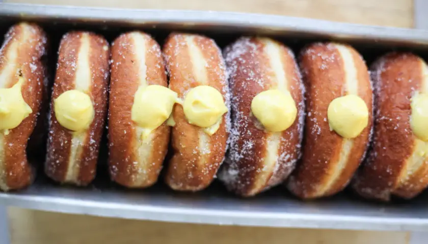 Una fila di bomboloni alla crema, cosparsi di zucchero, pronti per essere gustati.