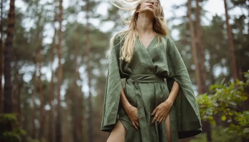 Kobieta w lnianej sukience w lesie. Włosy rozwiane przez wiatr, zmysłowa fotografia mody.